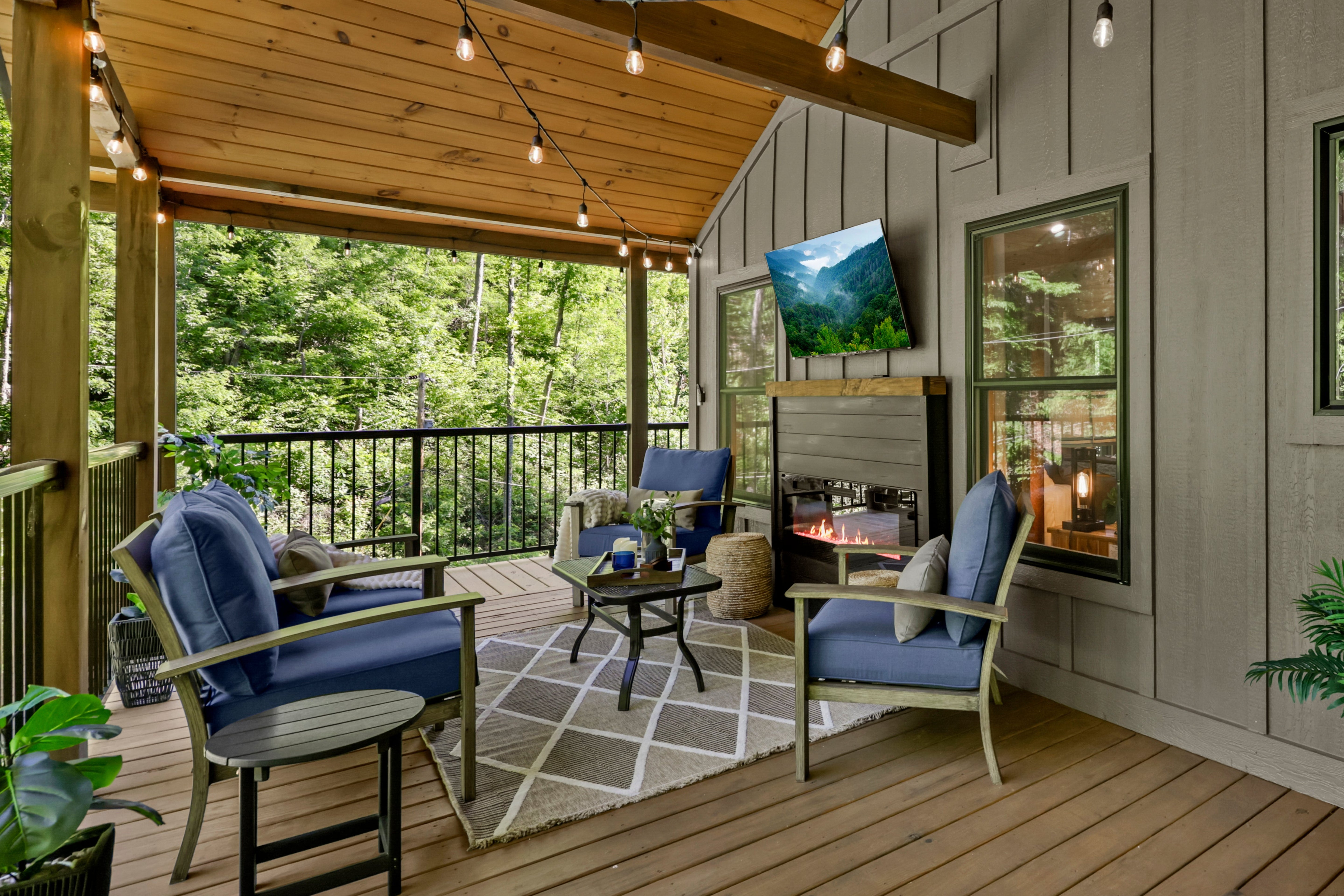 Outdoor living space with blue chairs, a fire pit, and large windows overlooking greenery.