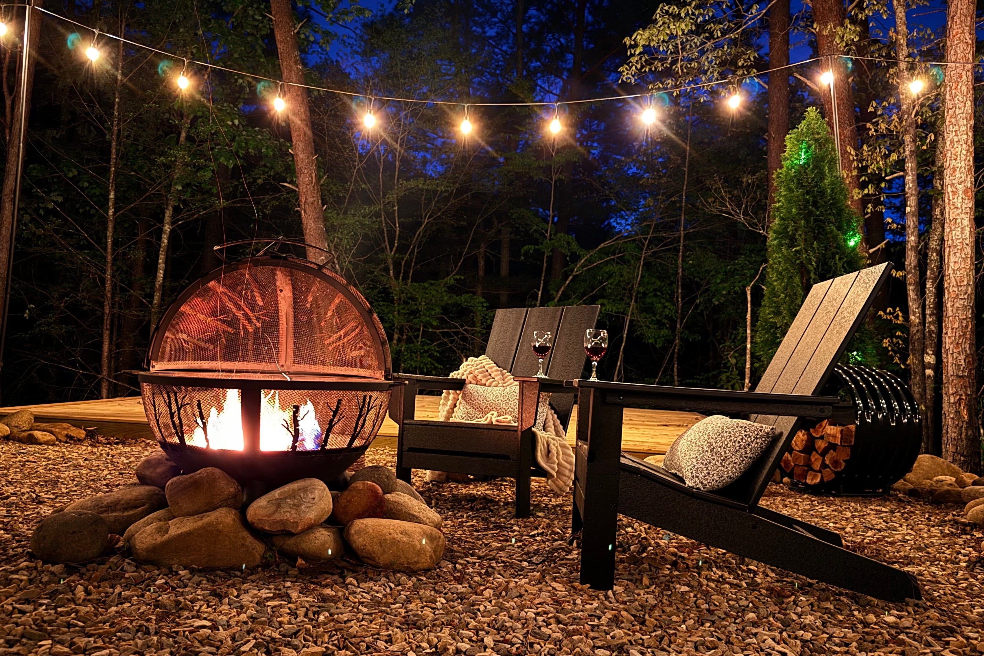 Outdoor evening setting with string lights, fire pit, and wooden chairs in a forested area at Villa Sol