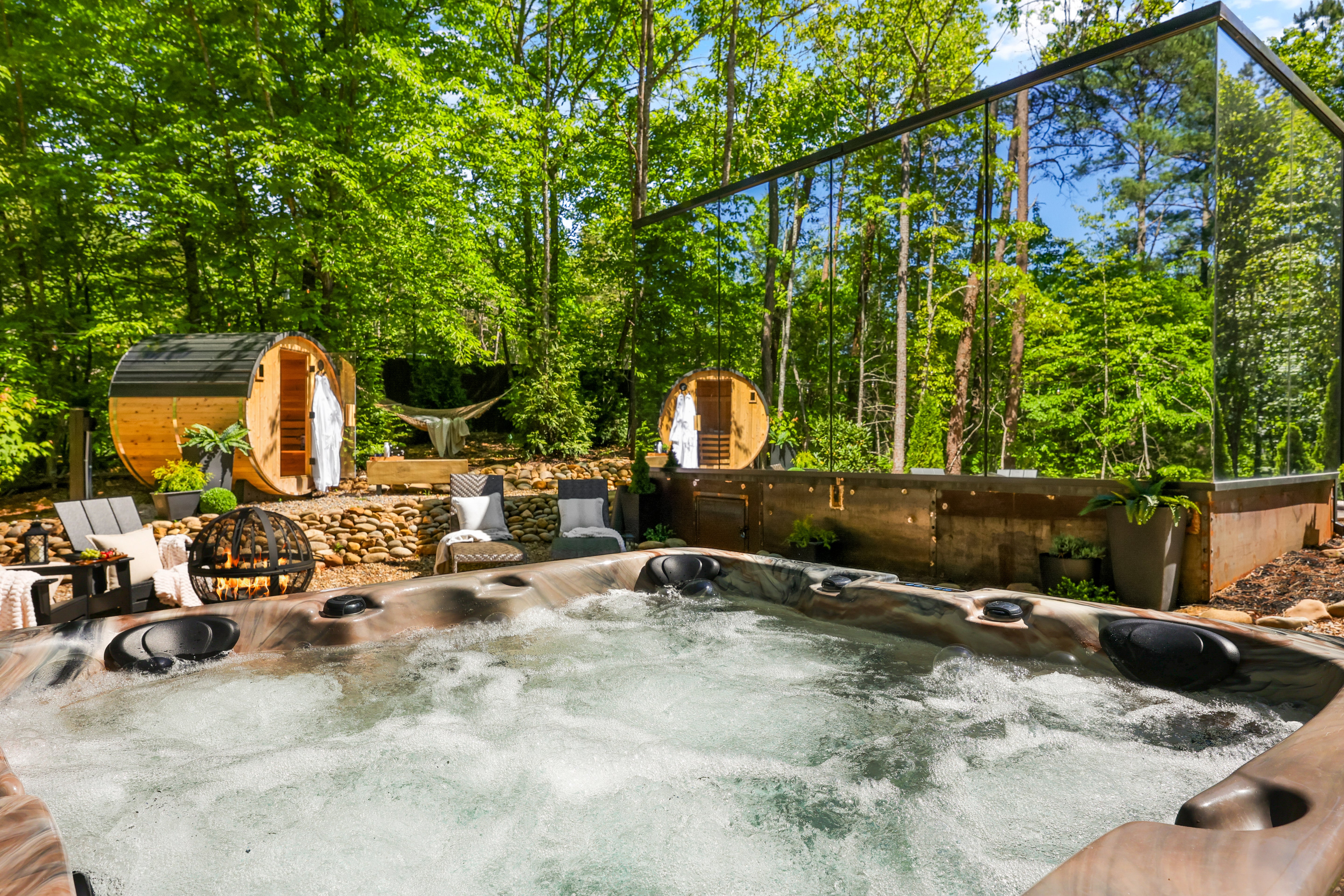 Hot tub in a wooded area with lounge chairs and wooden structures.